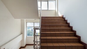 Una escalera con peldaños marrones y barandilla de metal, que lleva a una plataforma con ventana.