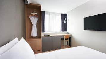 Una habitación de hotel moderna con cama, escritorio, silla, armario y televisor.