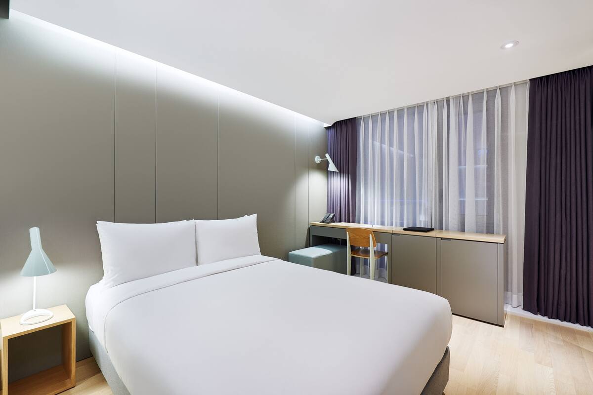 A modern hotel room with a large bed, a desk, and a chair.