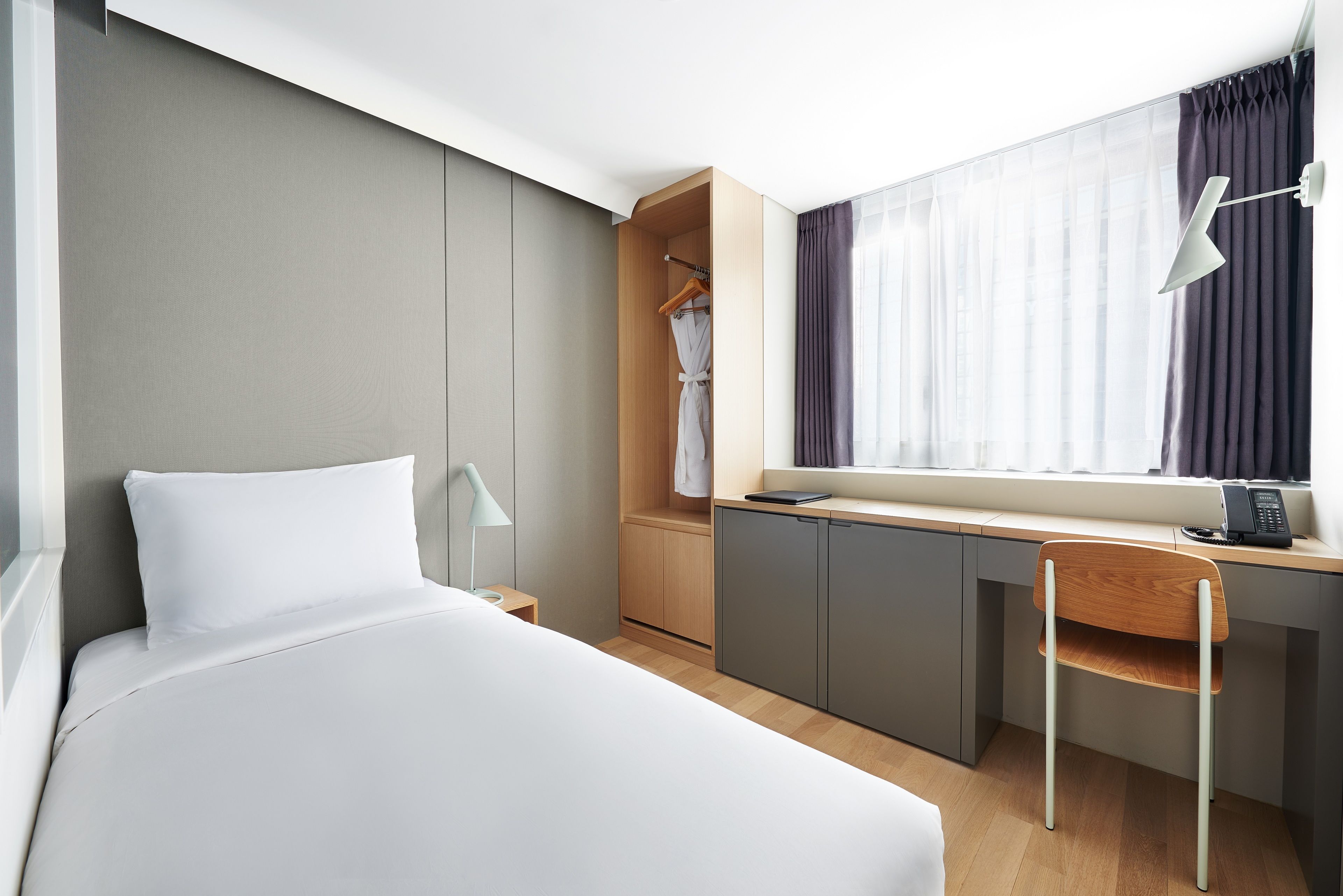 A hotel room with a bed, a desk with a chair, a wardrobe, and a window with curtains.