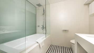 A modern bathroom with a glass-enclosed shower, a white bathtub, and a black and white patterned floor.