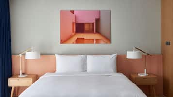 A hotel room with a large bed, two bedside tables with lamps, a wall-mounted picture, and a wooden door.