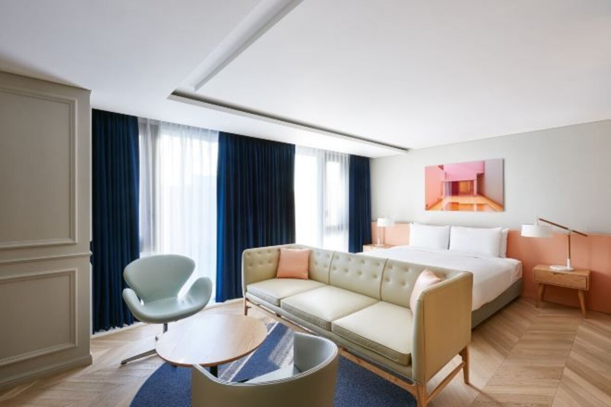 Ett hotellrum med en säng, en soffa, en stol, ett litet bord och en lampa.