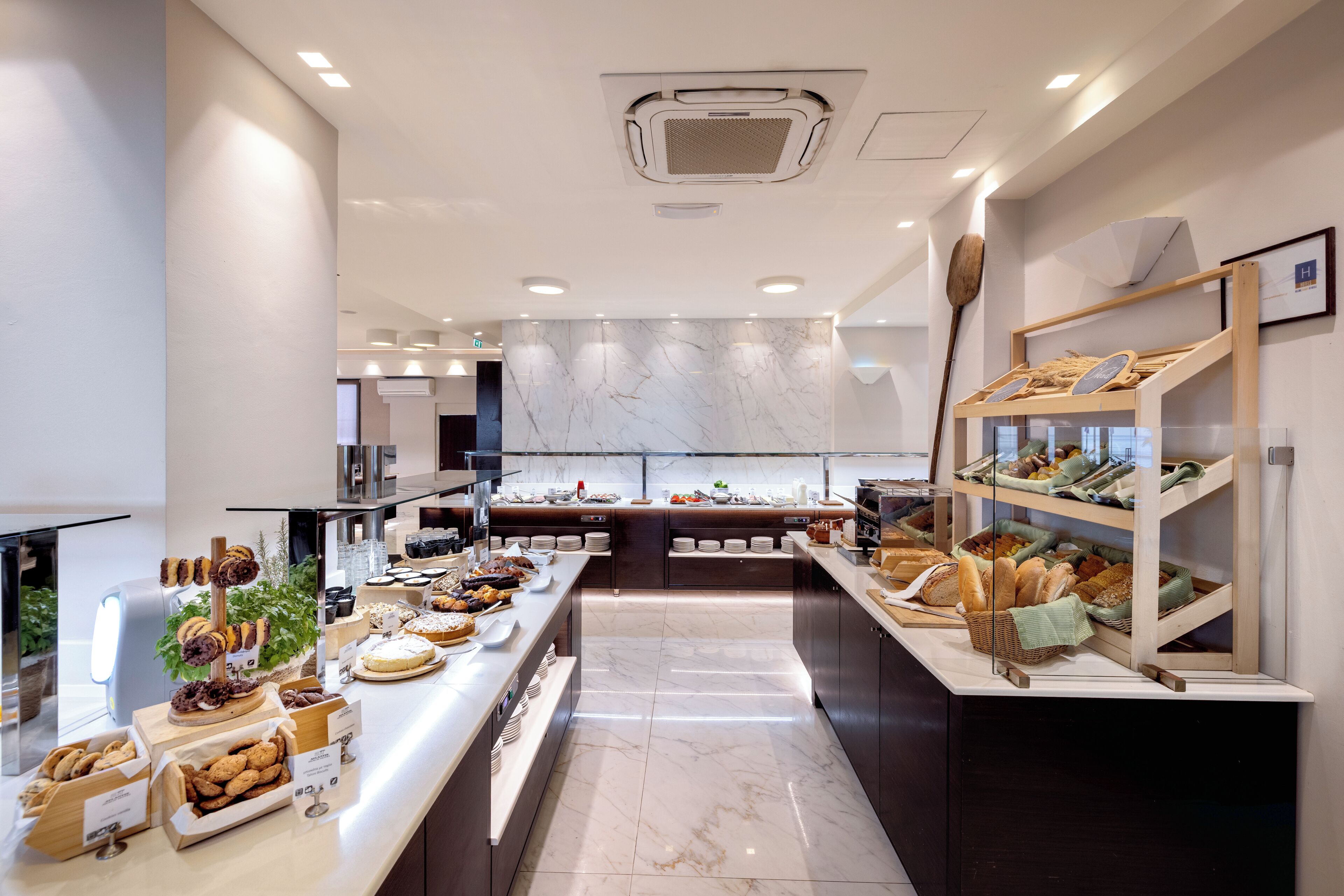 A modern kitchen with marble countertops, a variety of baked goods, and a wooden bread display.