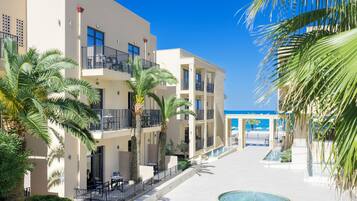 Un hotel moderno con varios balcones, palmeras y una zona de piscina central.