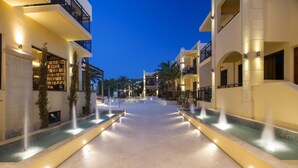 Un patio de hotel con piscina central, rodeado de edificios con balcones e iluminación exterior.