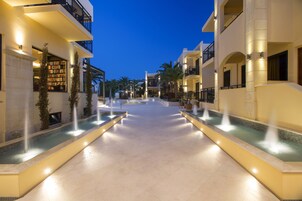 Un patio de hotel con piscina central, rodeado de edificios con balcones e iluminación exterior.