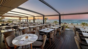 Un área de comedor al aire libre con mesas y sillas, con vista al océano al atardecer.