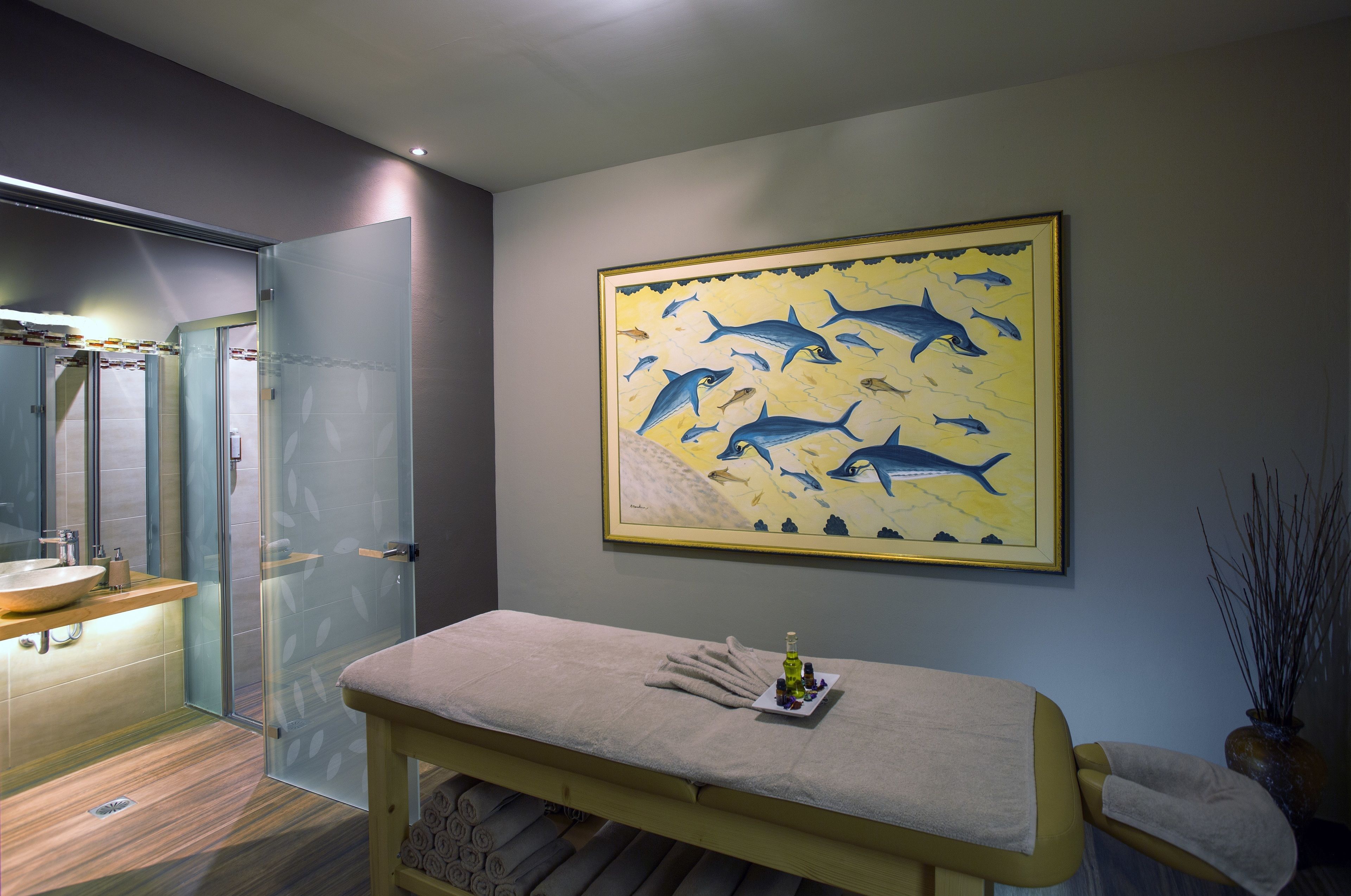 A modern bathroom with a glass shower, a sink, and a massage table with towels and a bottle.