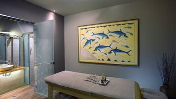 A modern bathroom with a glass shower, a sink, and a massage table with towels and a bottle.