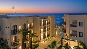 Un hotel de varios pisos con balcones, zona de piscina y vista al mar al atardecer.