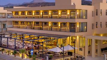 Un hotel moderno con varios pisos, asientos al aire libre y vistas a montañas al fondo.