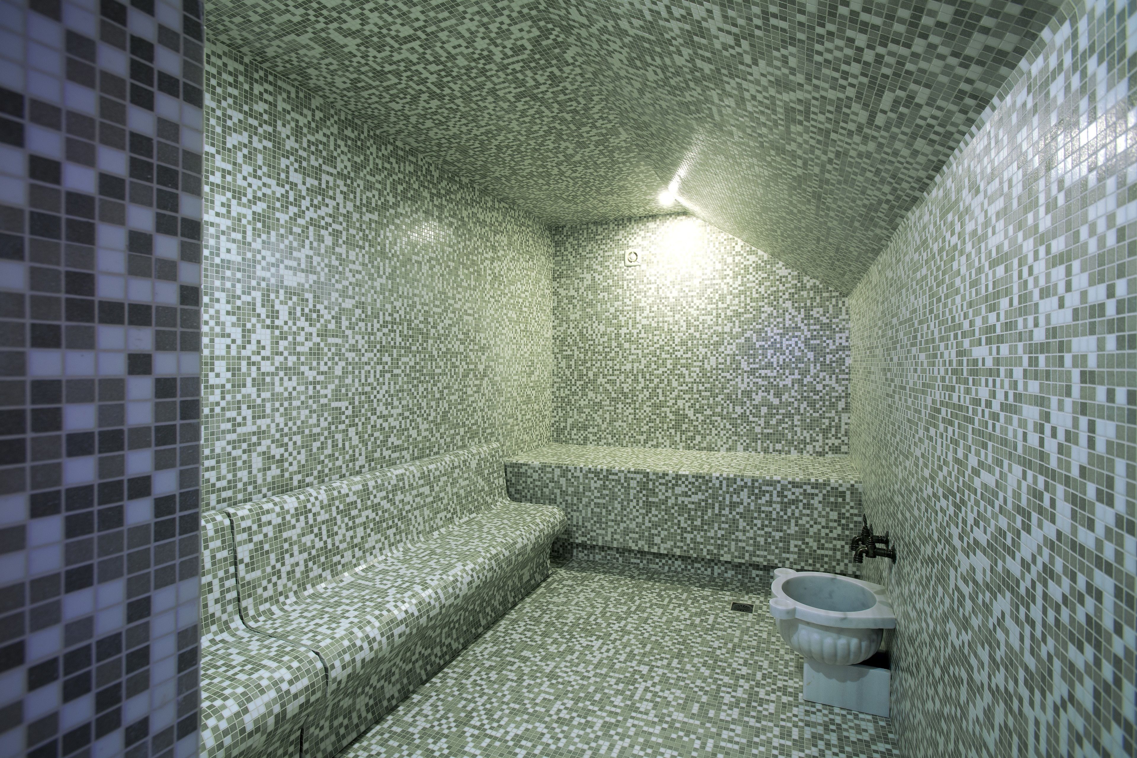 Een badkamer met betegelde muren en vloer, een toilet en een bankje.