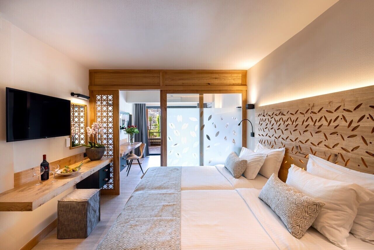 Ein modernes Schlafzimmer mit einem großen Bett, einem an der Wand montierten Fernseher, einer Holzbank und einer dekorativen Wandverkleidung.