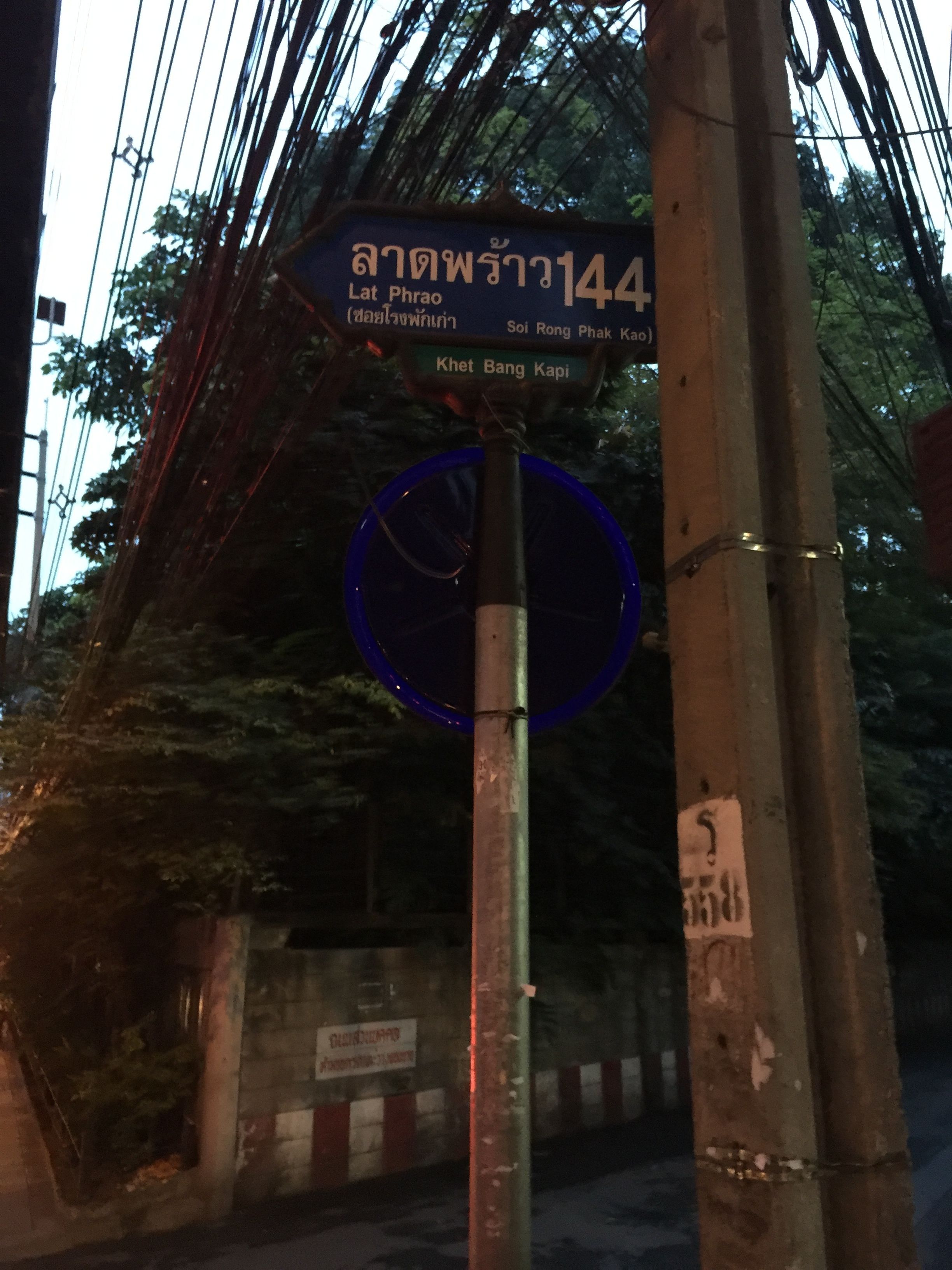 A street sign with Thai text and a blue circular sign below it.