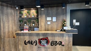 A reception desk with a wooden finish, a sign for Korean BBQ Buffet, and a Christmas tree decoration. - Mall Suites Hotel (Bangkok)