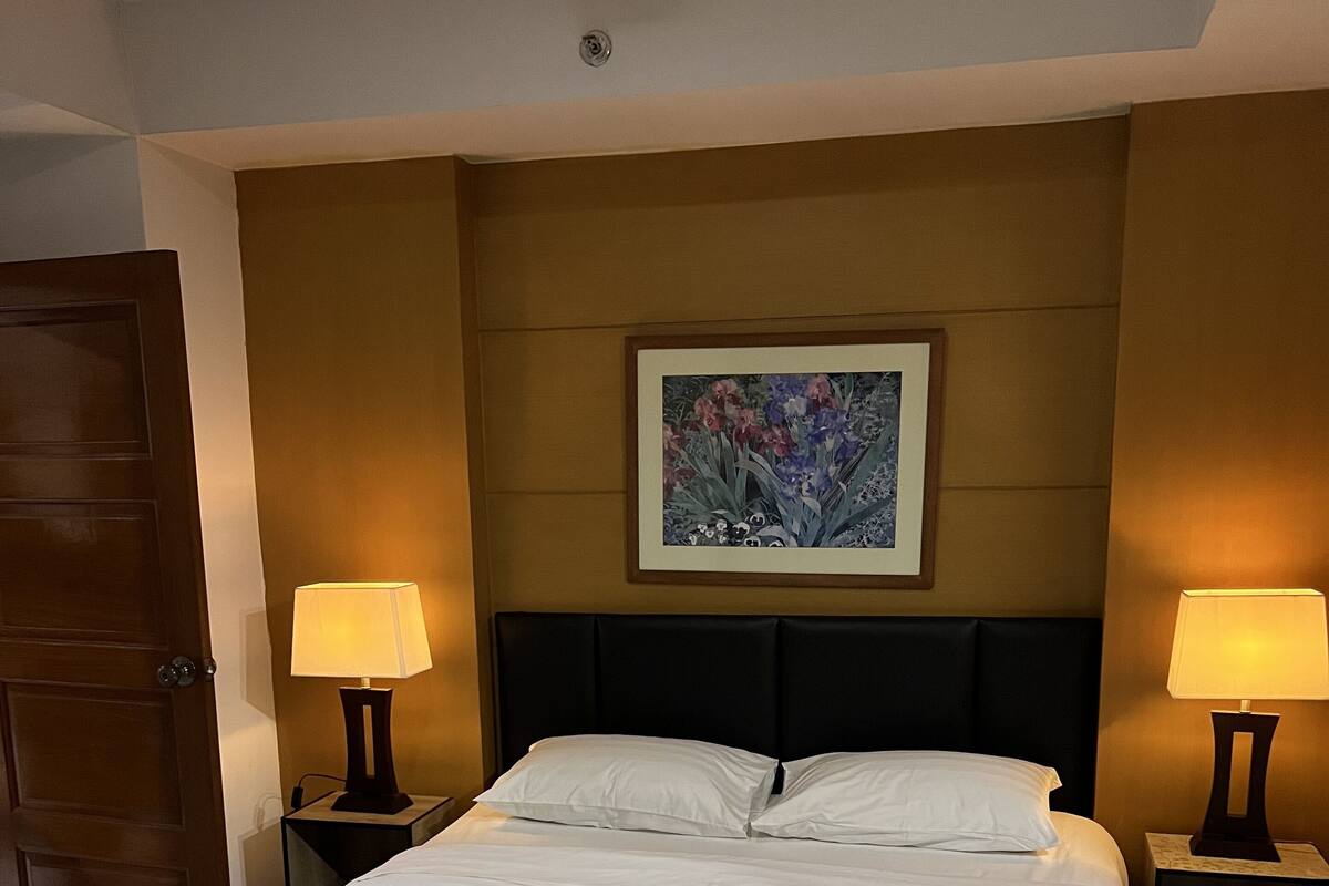 A neatly made bed with white linens, a dark headboard, and two bedside lamps.