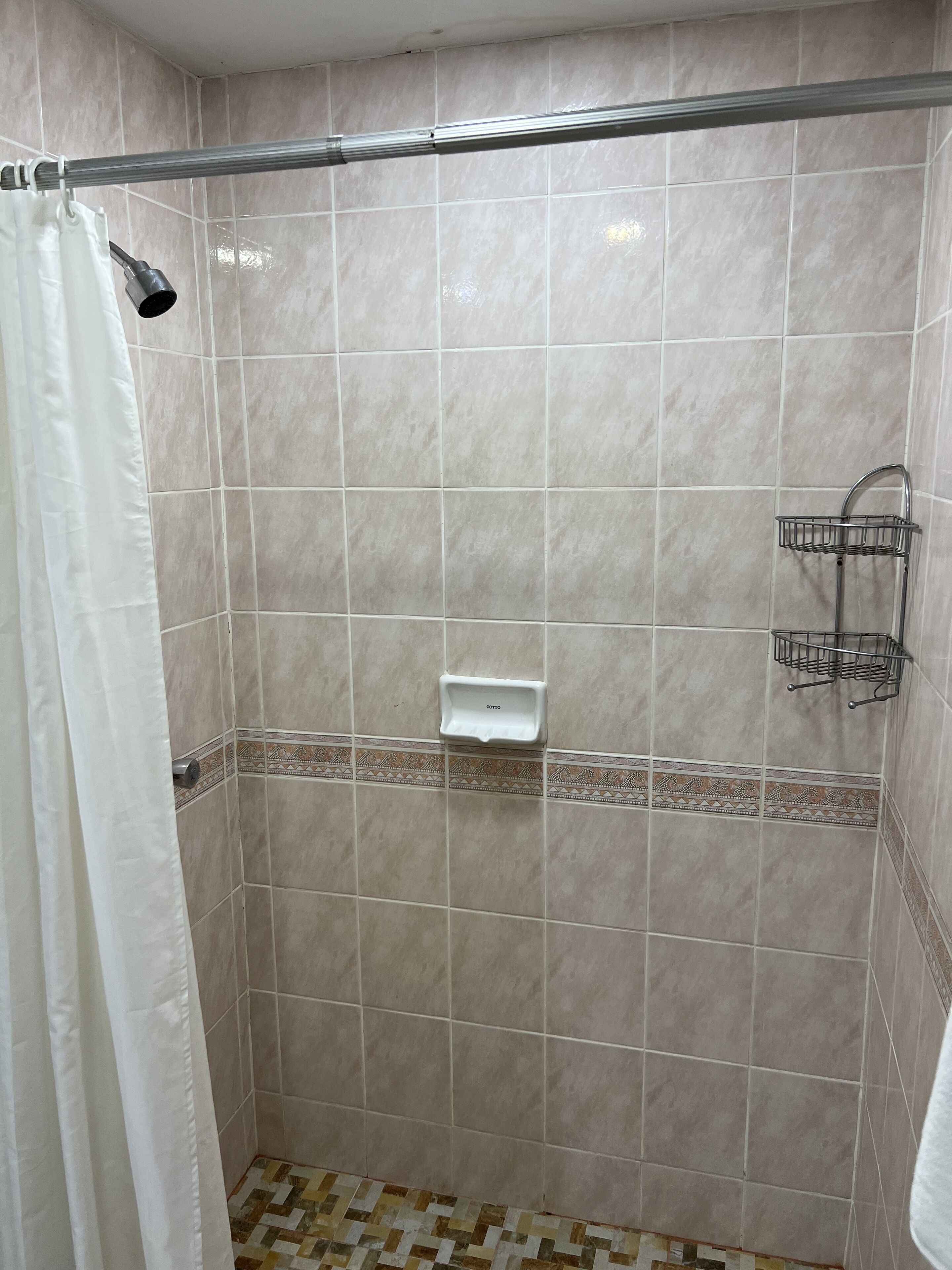 Un espacio de ducha con azulejos color beige, una cortina de baño y un jabonera.