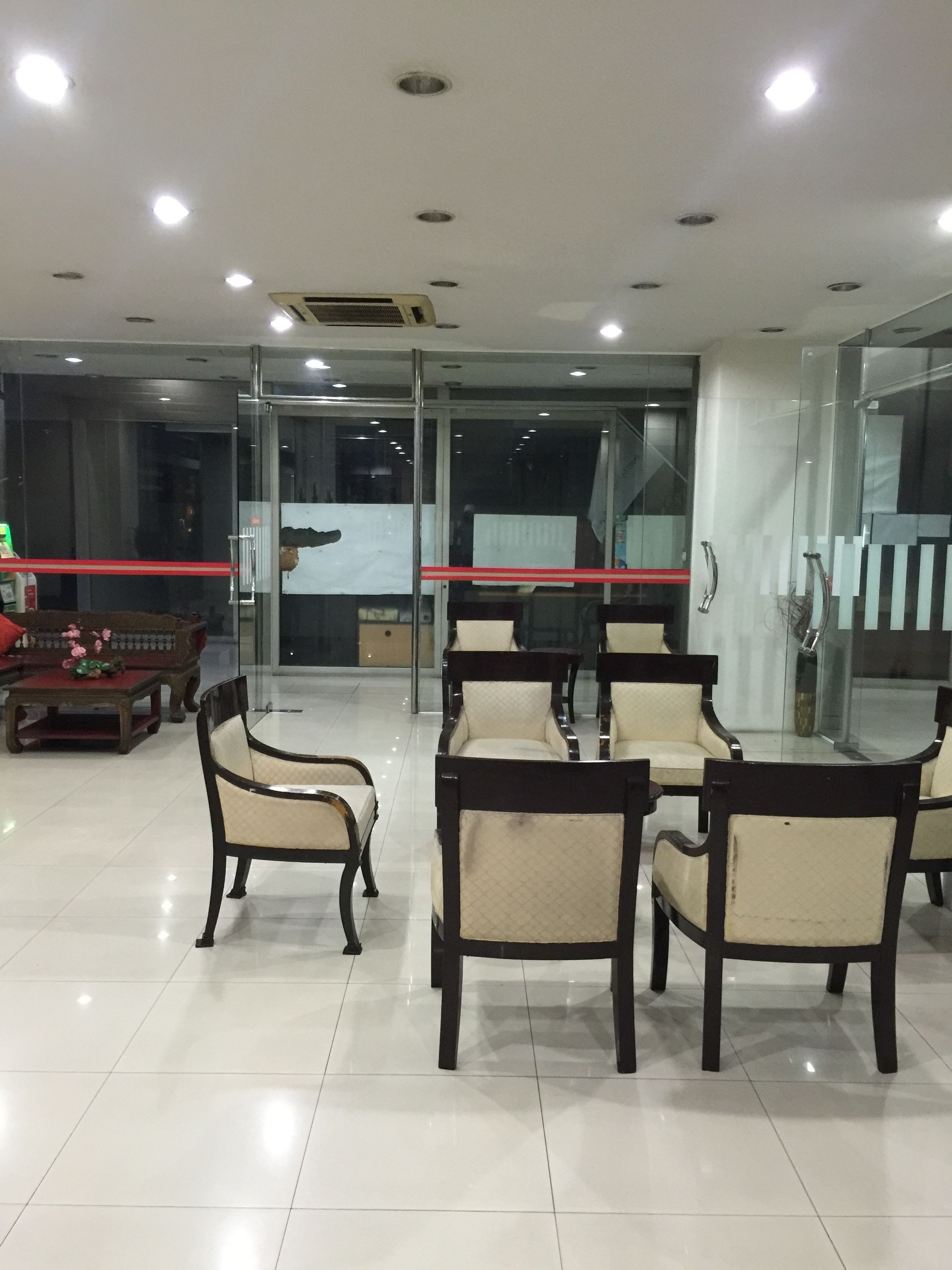 A modern hotel lobby with a glass partition, a wooden sofa, and several chairs arranged around a table.