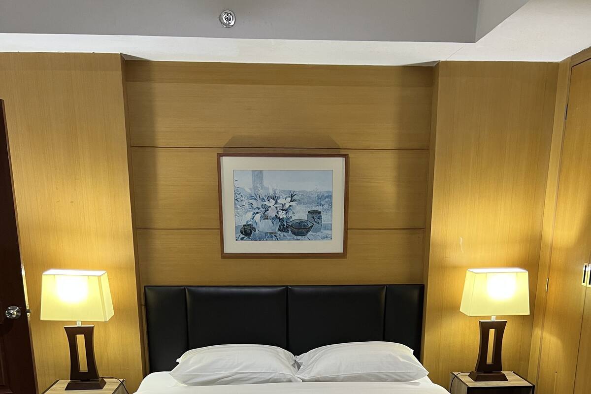 A neatly made bed with white linens in a room with wooden paneling and a framed picture on the wall.