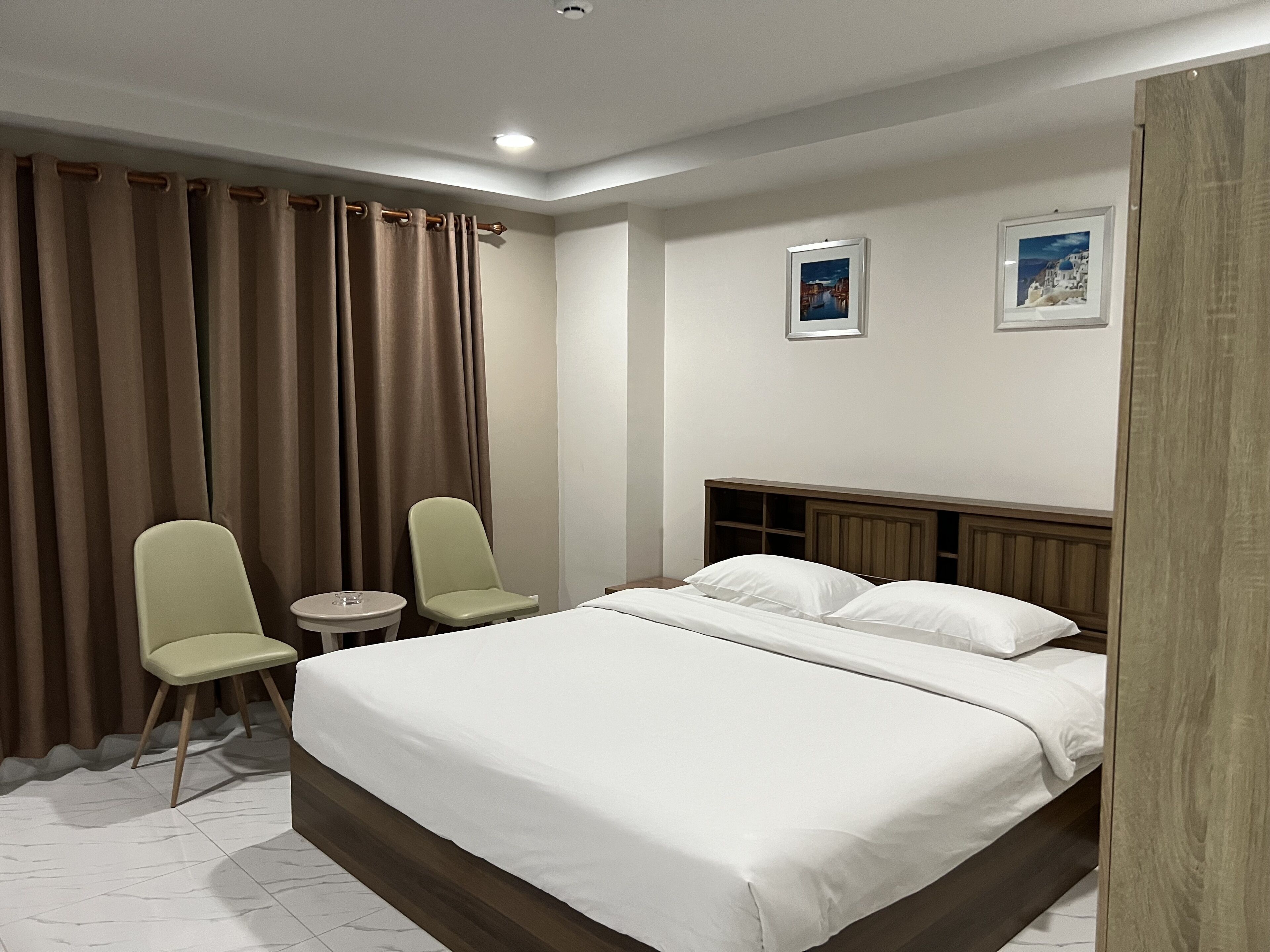 A hotel room with a large bed, two chairs, a small table, and two framed pictures on the wall.