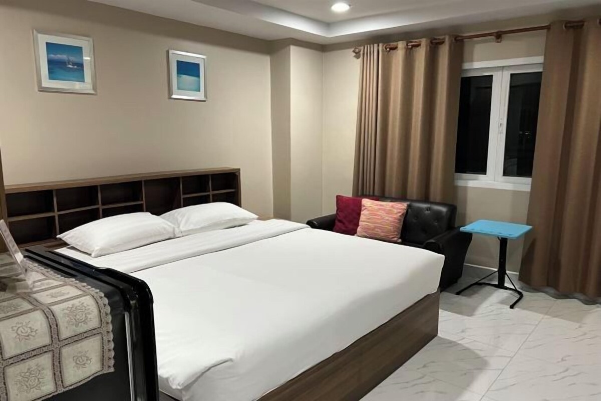A hotel room with a bed, a nightstand, a small table, and a window with curtains.