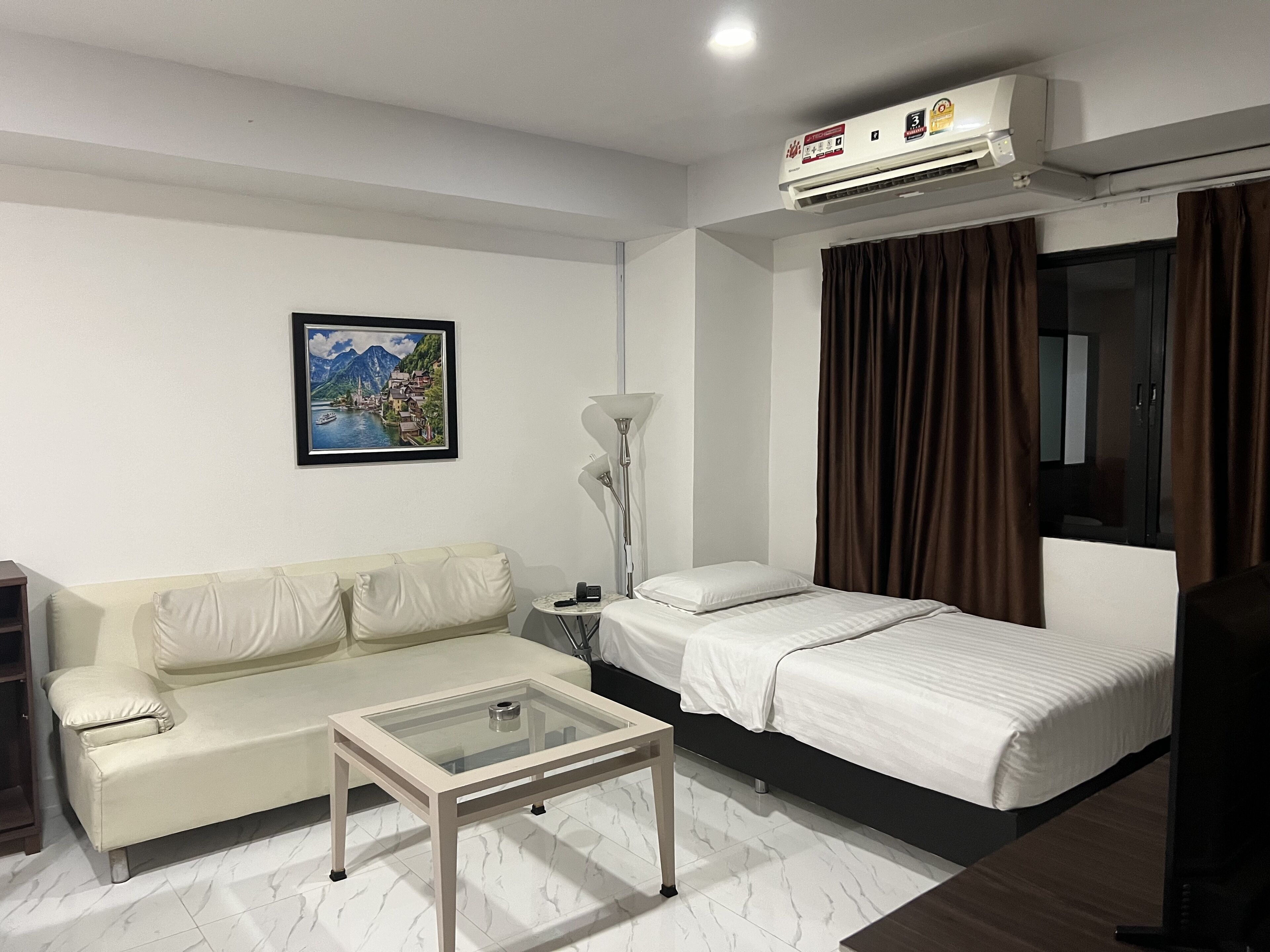 Een hotelkamer met een bed, een bank, een glazen salontafel, een lamp, een schilderij aan de muur en een airconditioning.