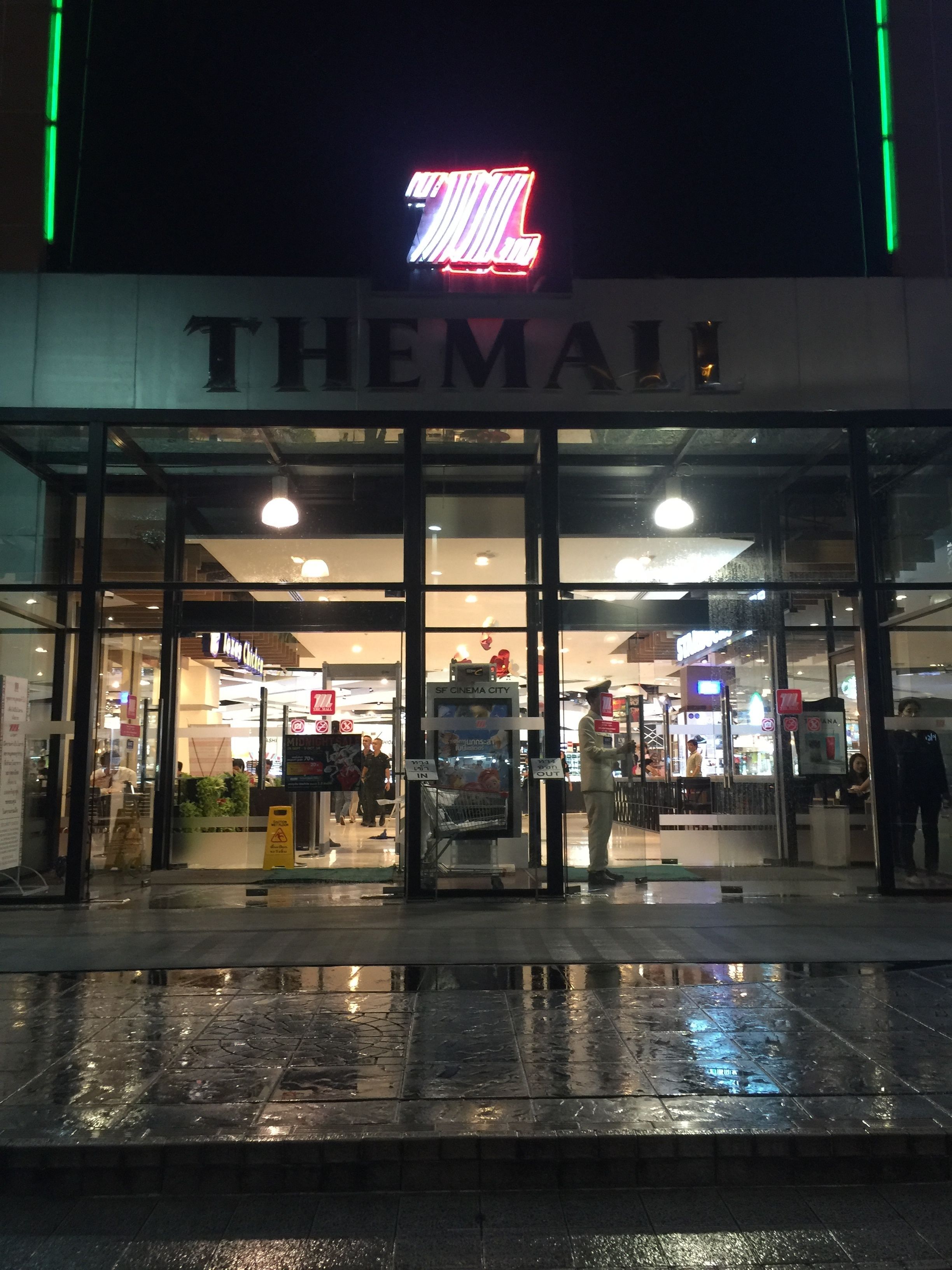 A cinema with a neon sign, glass doors, and a wet pavement.