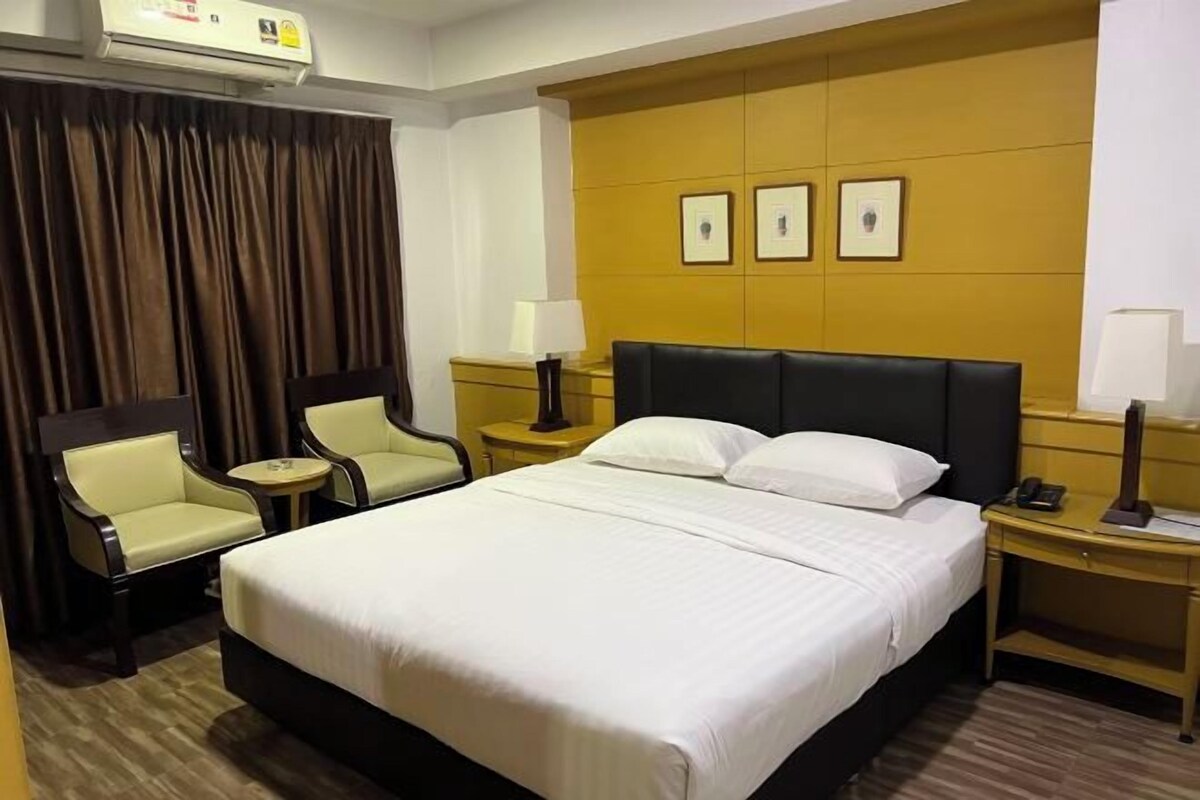 A hotel room with a large bed, two armchairs, a bedside table with a lamp, and a wall-mounted air conditioner.
