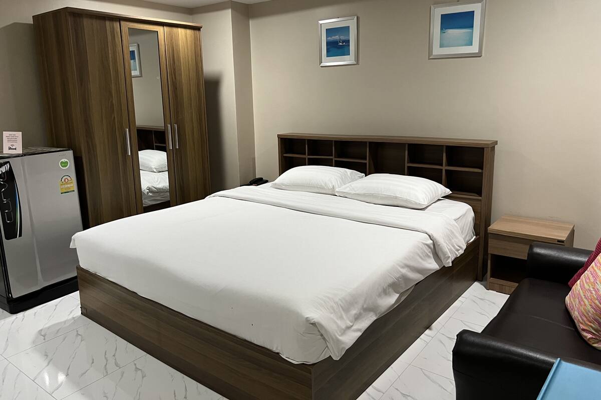 A hotel room with a large bed, a wardrobe, a bedside table, and a refrigerator.