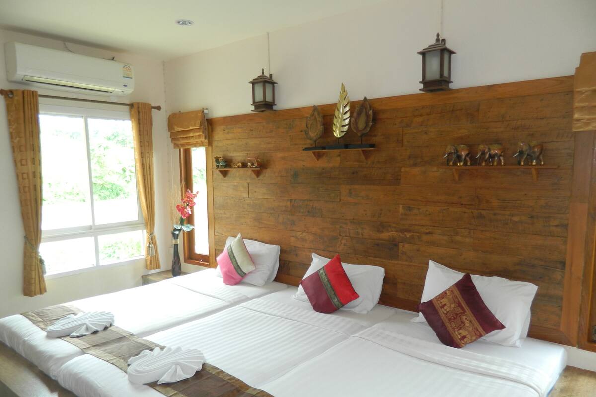 A hotel room with two beds, wooden headboard, decorative wall sconces, and a window with curtains.