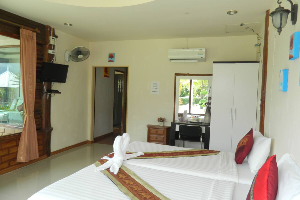 A hotel room with a bed, a desk, an air conditioning unit, a television, and a window with curtains.