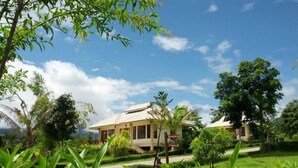 A bungalow-style hotel with a thatched roof, surrounded by lush greenery and palm trees. - Pai Iyara Resort (Pai)