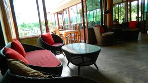 A spacious outdoor seating area with wicker furniture and a glass table, overlooking a lush garden. - Pai Iyara Resort (Pai)