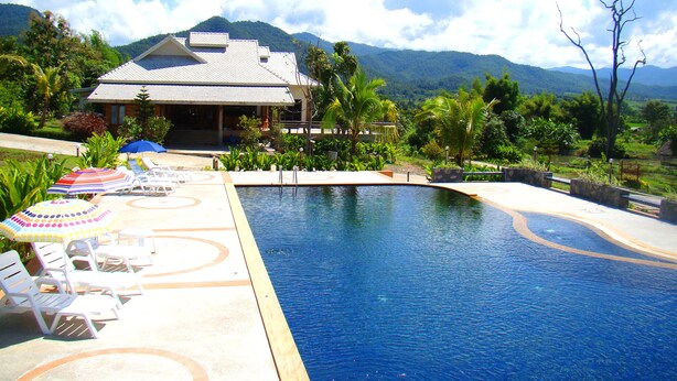 A swimming pool with lounge chairs and umbrellas, surrounded by lush greenery and a mountain in the background. - Pai Iyara Resort (Pai)