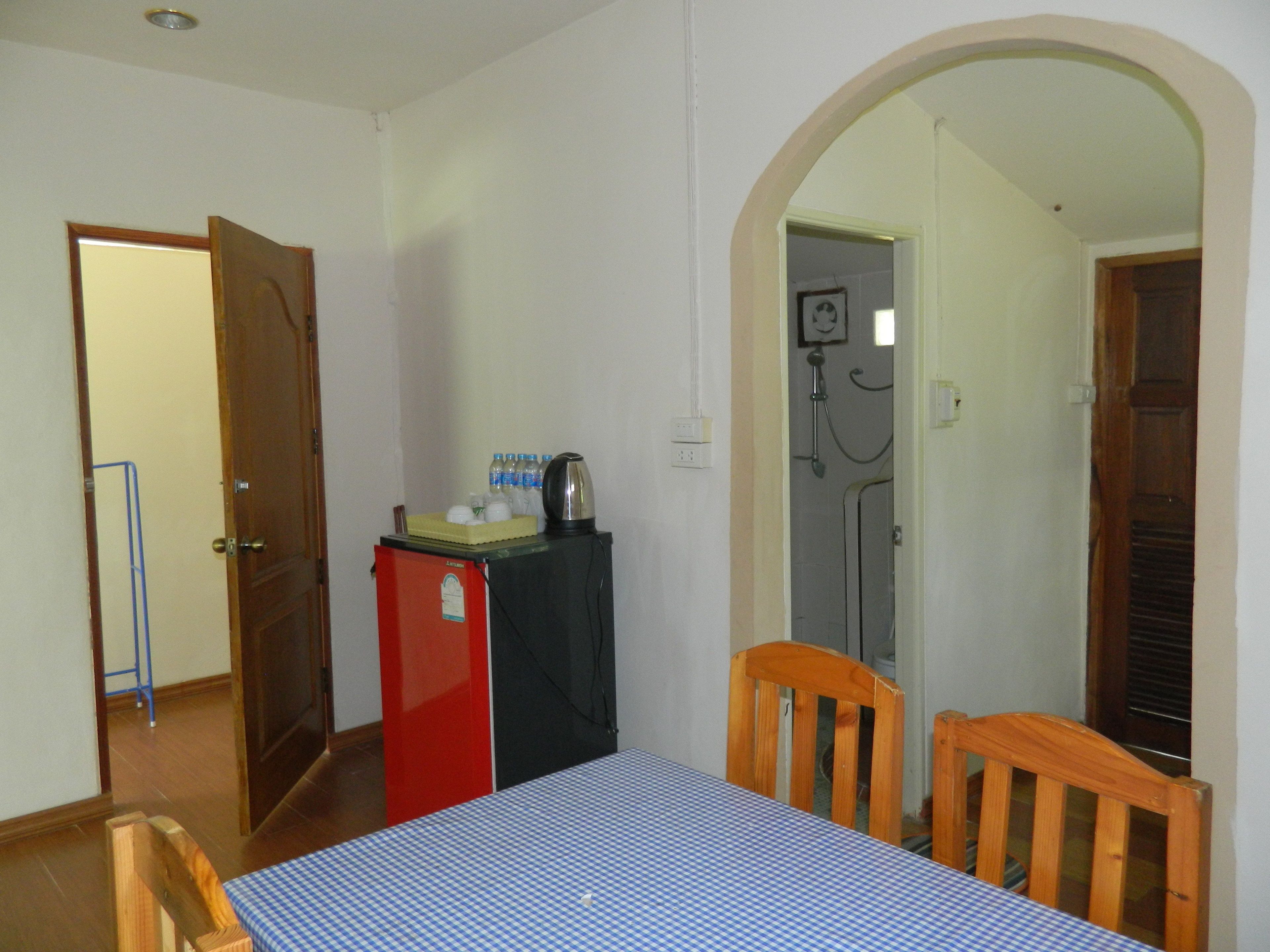 Una habitación con cama, un refrigerador pequeño, una mesa con mantel a cuadros y una silla de madera.