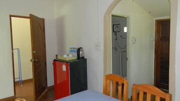 Una habitación con cama, un refrigerador pequeño, una mesa con mantel a cuadros y una silla de madera.