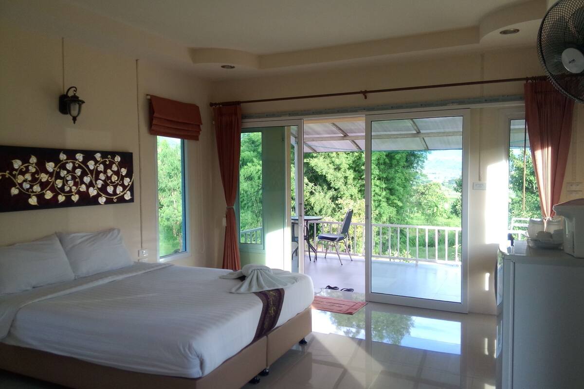 A bedroom with a bed, a nightstand, a fan, and a view of the outdoors.