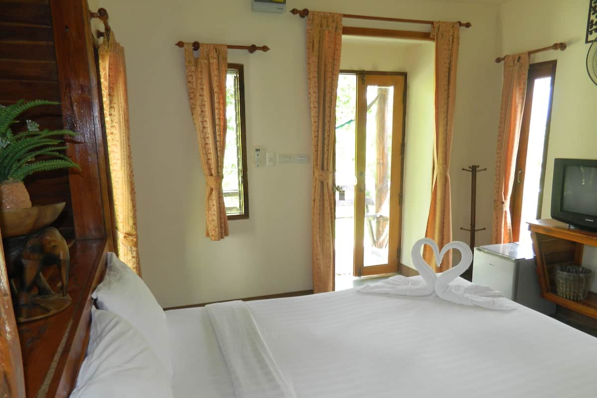 A hotel room with a bed, curtains, a television, a small table, and a plant.