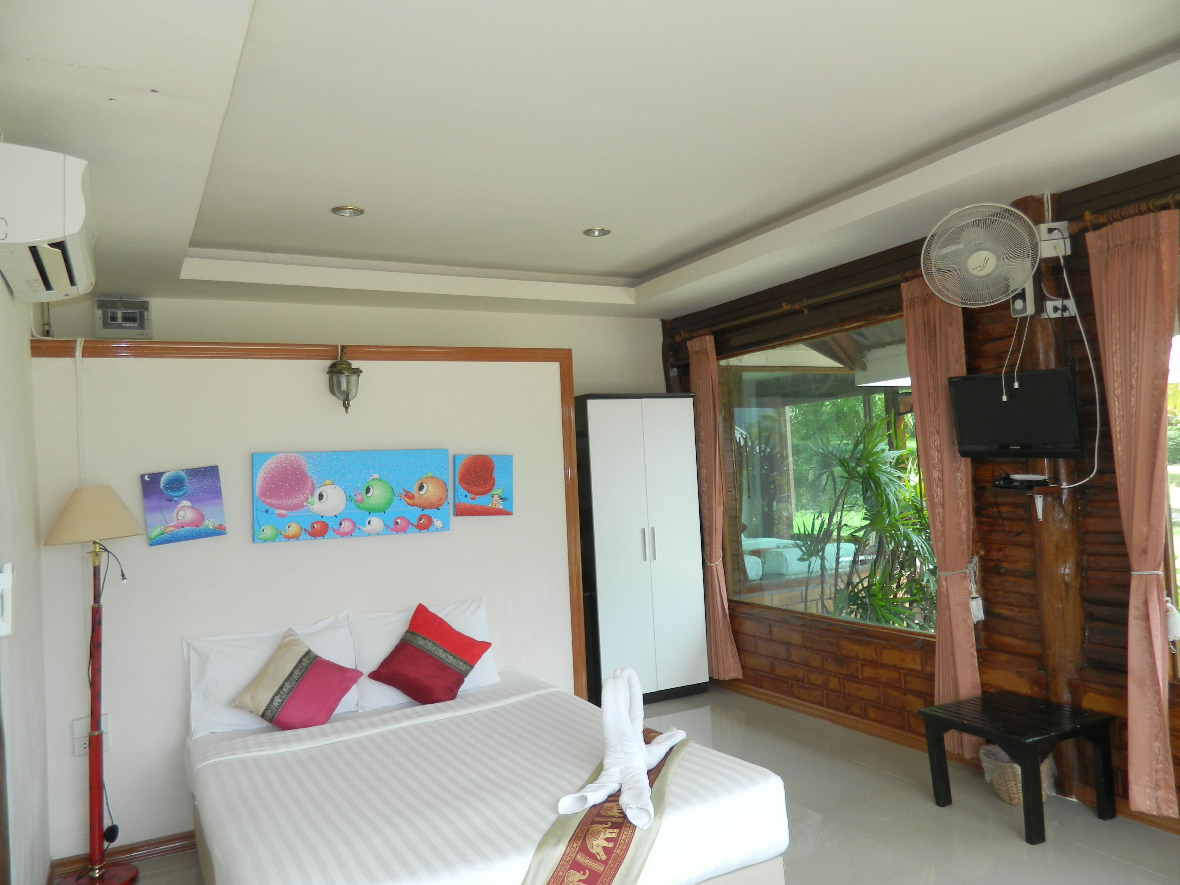 Una habitación de hotel con cama, escritorio, televisor y ventana con cortinas.