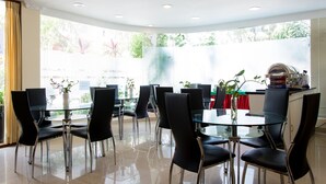 A modern dining area with glass tables and black chairs, a chandelier, and a view of greenery outside. - BEACH PALACE HOTEL (Hulhumalé)