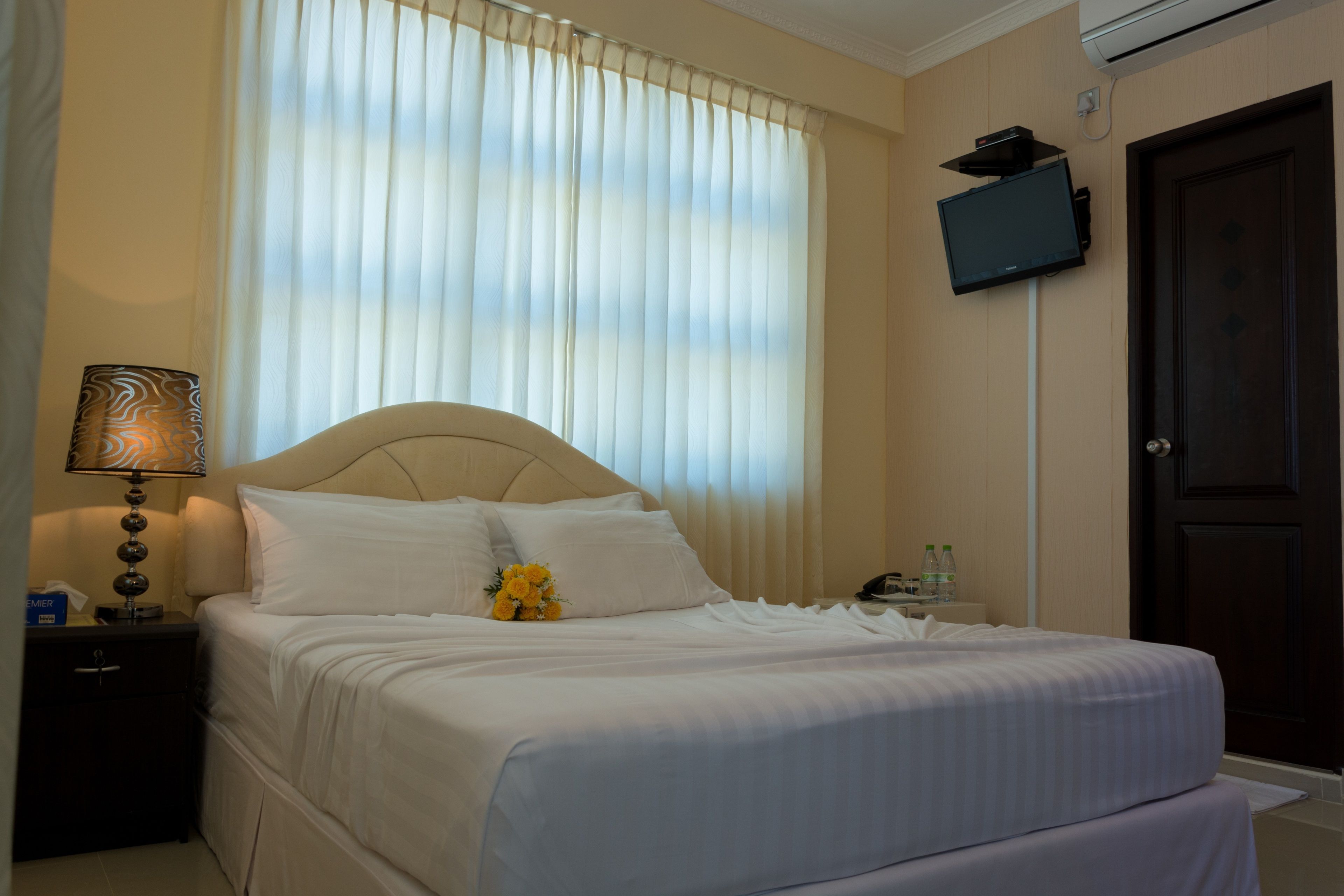 A hotel room with a bed, a nightstand, a lamp, a television mounted on the wall, and a door.