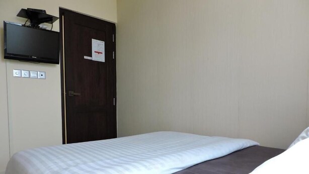 Una habitación de hotel con cama, televisor montado en la pared y una puerta con un aviso.