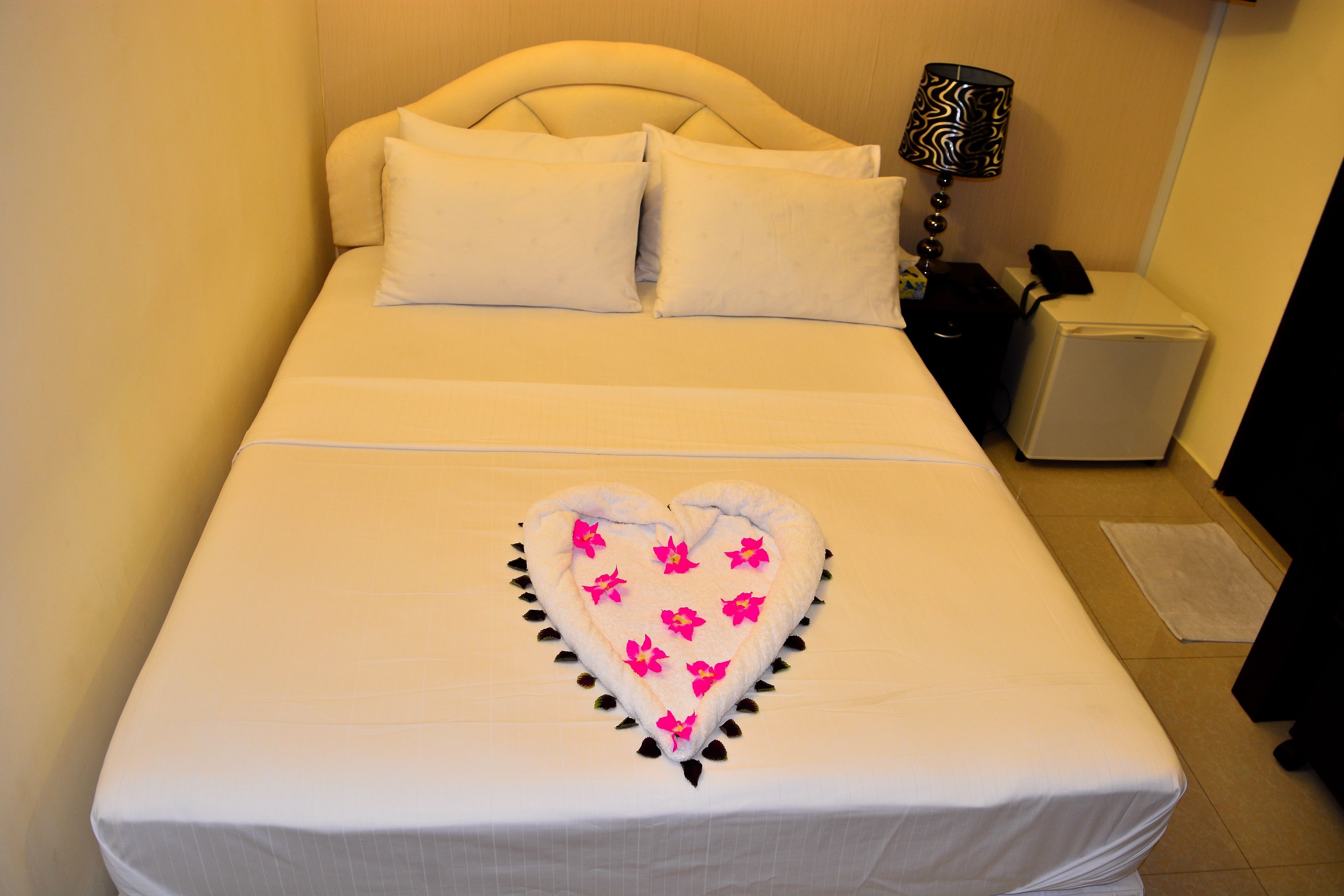 A neatly made bed with a heart-shaped towel decoration and pillows.