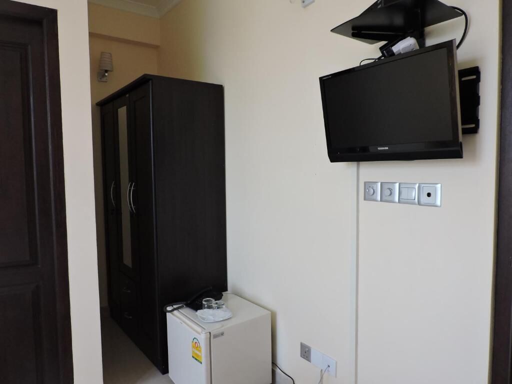 Una habitación con un armario de madera oscura, un electrodoméstico pequeño blanco y un televisor de pantalla plana montado.