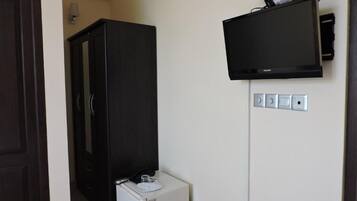 Una habitación con un armario de madera oscura, un electrodoméstico pequeño blanco y un televisor de pantalla plana montado.