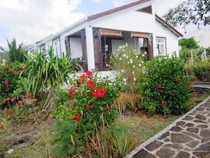 A two-story house with a white exterior and brown trim. It features a covered porch with wooden lattice. - Residence Foulsafat (Rodrigues Island)