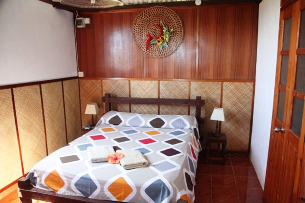 A neatly made bed with a patterned bedspread, two bedside lamps, and a decorative wall hanging.