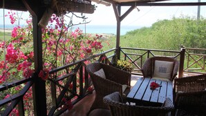 A covered outdoor seating area with wicker furniture and a table, overlooking a scenic landscape with pink flowers and a view of the sea. - Residence Foulsafat (Rodrigues Island)