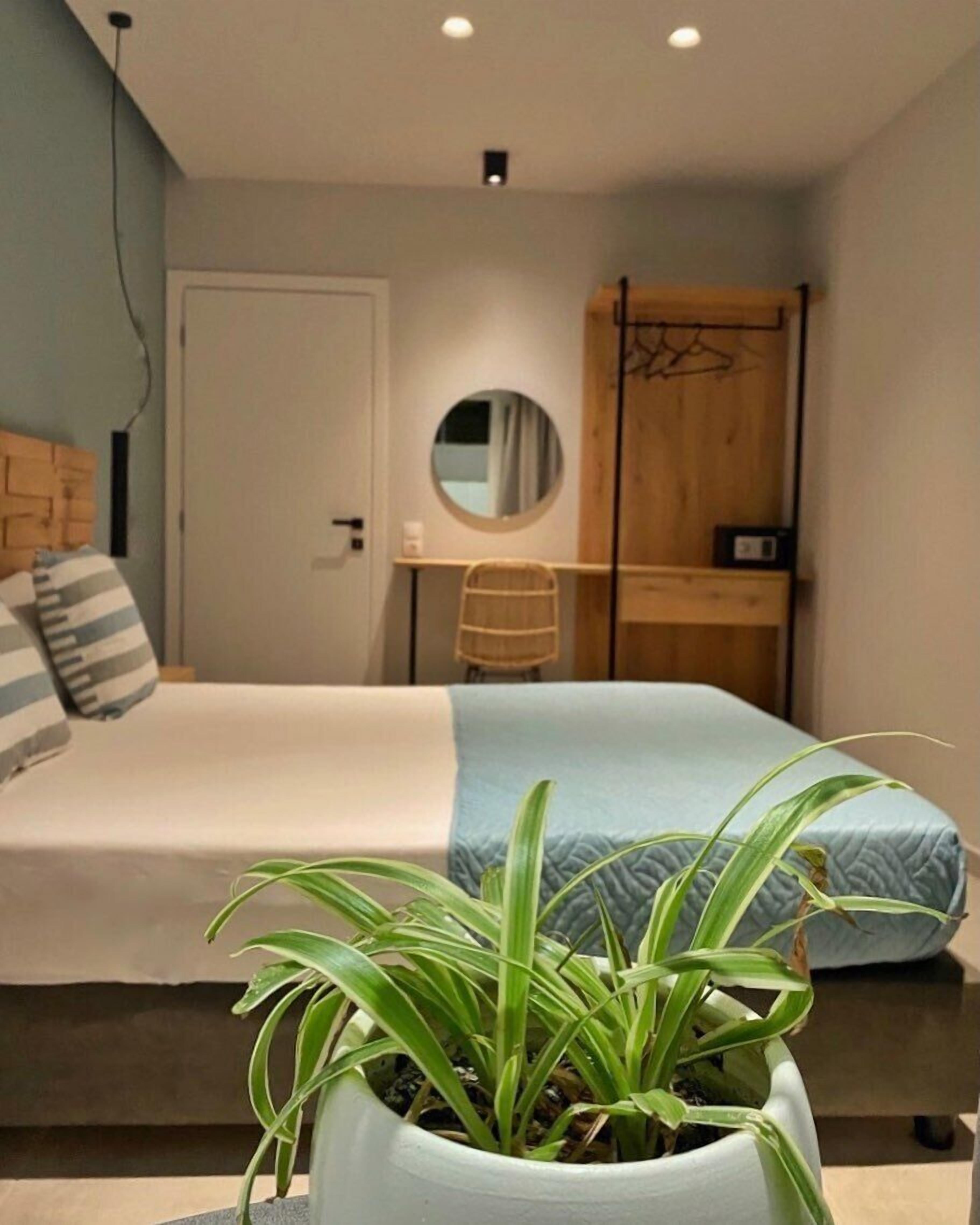 Un dormitorio con cama, escritorio, silla y planta en maceta.
